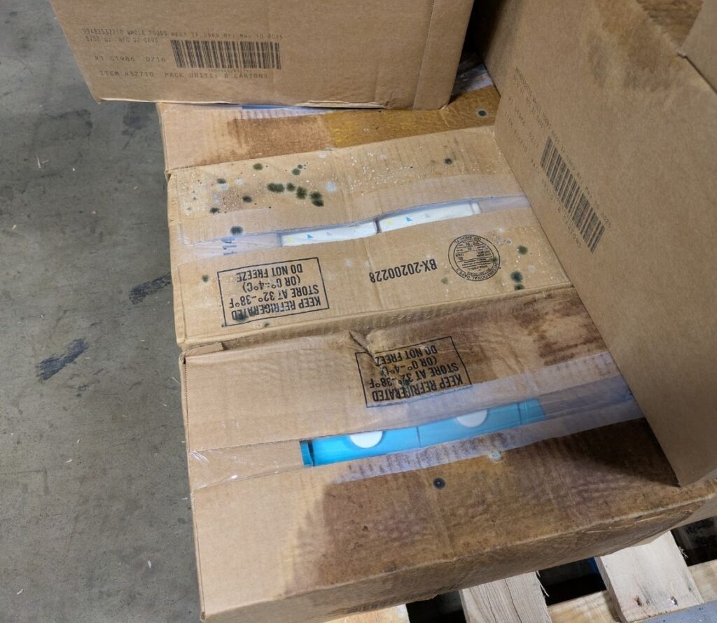 Workers restacking and shrink wrapping damaged pallets in a warehouse rework service area.